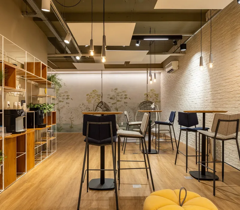 Área de recepção com estação de café, prateleiras com plantas e mesas altas