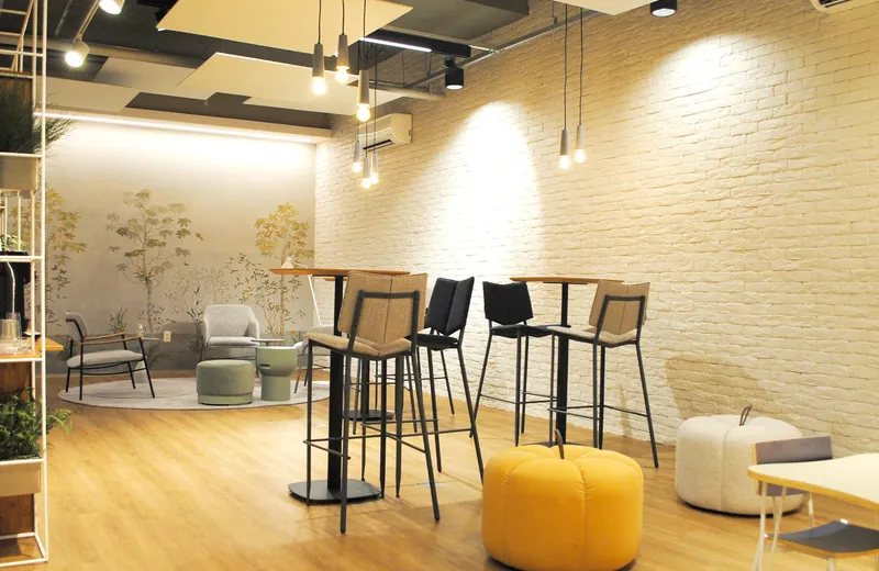 Recepção com mesas altas, parede de tijolinho e lounge ao fundo